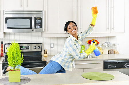 Woman wearing yellow rubber gloves in the kitchen holding a sponge and cleaning spray bottle